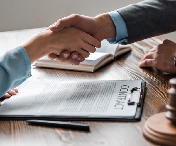 cropped shot of lawyer and client shaking hands above contract